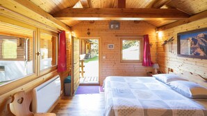 A wooden cabin room with a bed, a window, a door, and a small staircase leading outside.