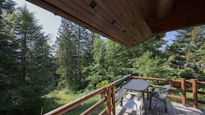 A wooden deck with a table and chairs, surrounded by a wooden railing, overlooking a forested area.