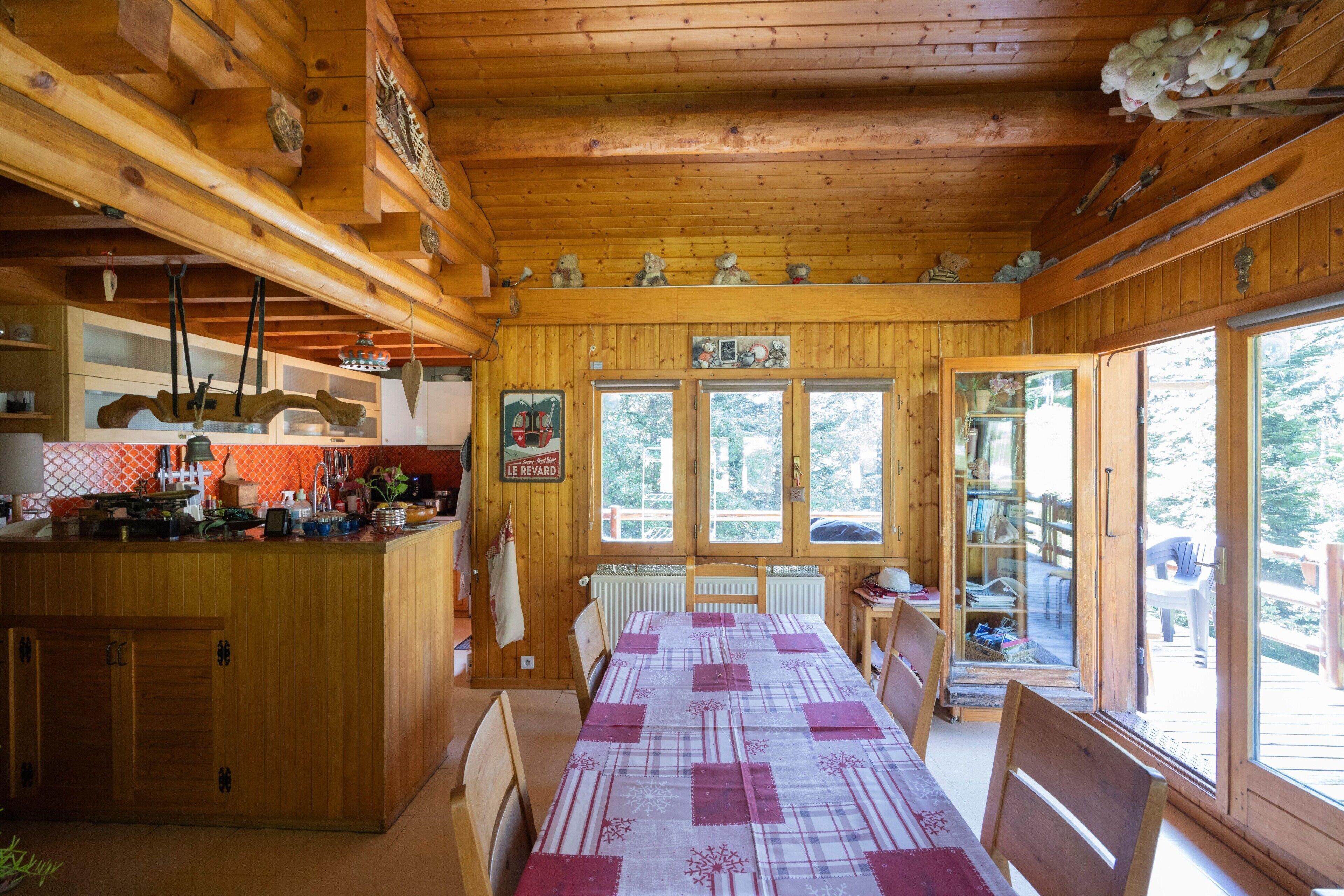 L’intérieur d’un chalet en bois comprend une table à manger, des chaises, un coin cuisine et de grandes fenêtres.