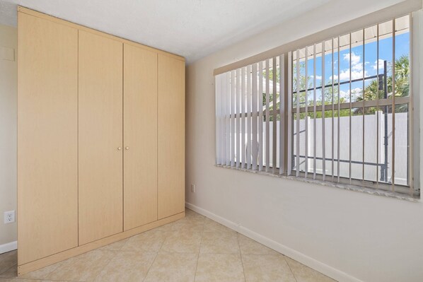Una habitación con un armario grande, una ventana con rejas y piso de baldosas.