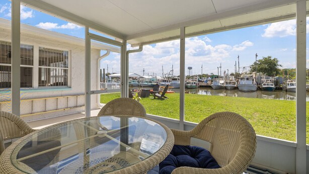 A glass-top table with wicker chairs, a view of boats on water, and a grassy area. - Gulf Access Getaway, 4 Kayaks, Dock, Fire Pit & Waterfront Fun, Boat Dock, FirePit, Bikes (Hernando Beach)