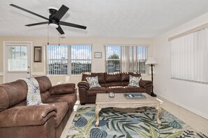 A living room with two brown leather sofas, a coffee table, a ceiling fan, and large windows with blinds. - Gulf Access Getaway, 4 Kayaks, Dock, Fire Pit & Waterfront Fun, Boat Dock, FirePit, Bikes (Hernando Beach)