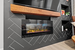 A modern living room with a fireplace, a mounted TV, and a wooden shelf.