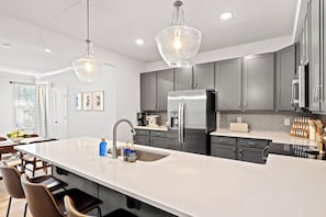 A modern kitchen with a large island, stainless steel appliances, and pendant lighting.