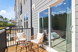 A deck with wicker chairs and a glass door leading to a covered patio.