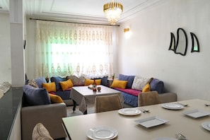 A dining area with a table set for four, a sofa with cushions, and a chandelier. - Luxury apartment 160 m² - Fès Al Amal (fes)