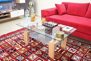 A living room with a glass coffee table, red sofa, patterned rug, and a chessboard. - Luxury apartment 160 m² - Fès Al Amal (fes)