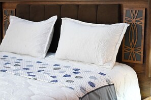 Ein Bett mit weißen Kissen und einer gemusterten Tagesdecke, ein Holz-Kopfteil und eine Wandverkleidung.