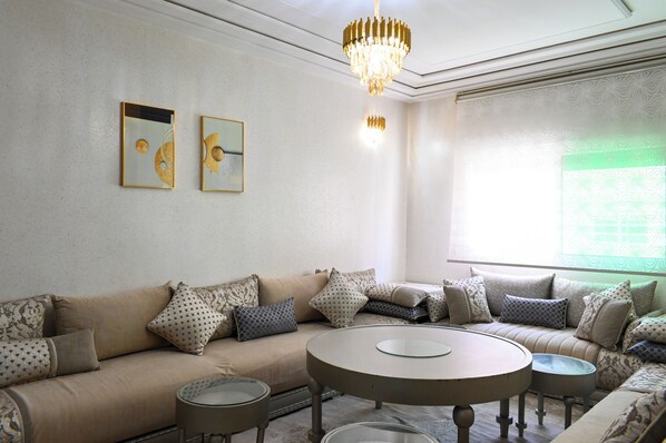 A living room with a beige sofa, patterned cushions, a round coffee table, and two wall-mounted artworks. - Luxury apartment 160 m² - Fès Al Amal (fes)
