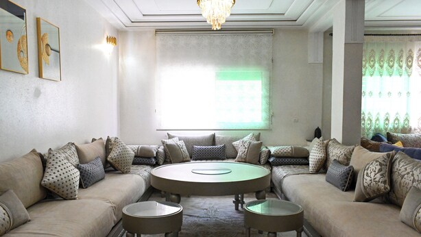 A living room with a beige sofa set, a round coffee table, and a patterned rug. - Luxury apartment 160 m² - Fès Al Amal (fes)