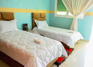 Two beds with white quilts, a brown headboard, a small bedside table with a plant, and a window with curtains. - Luxury apartment 160 m² - Fès Al Amal (fes)