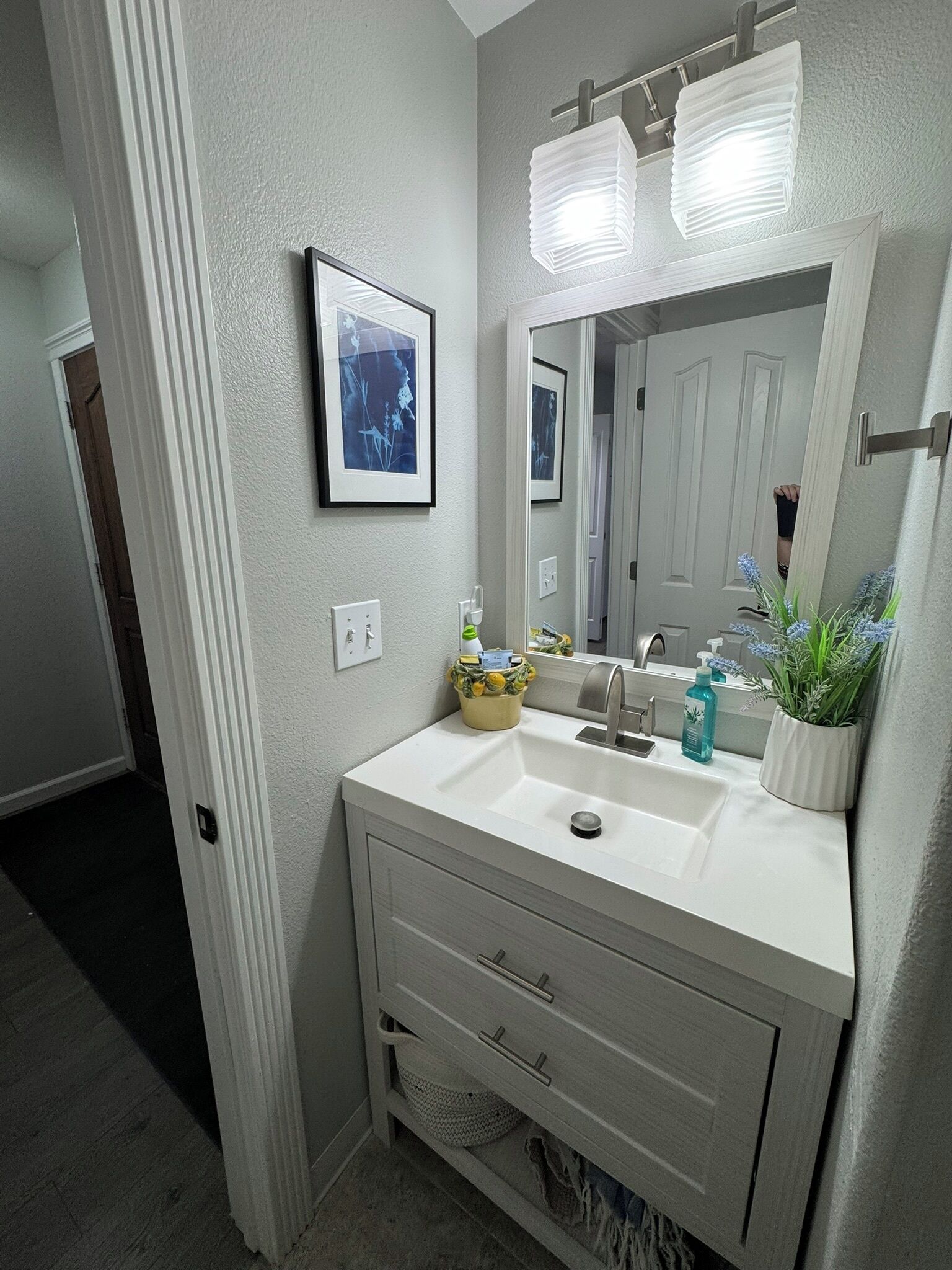 A bathroom with a white vanity, a sink, a mirror, and a framed picture on the wall.