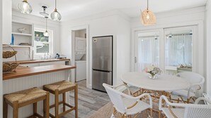 A modern kitchen with white cabinetry, a stainless steel refrigerator, and a round dining table with white wicker chairs. - NEW Twin Tides Retreat-steps to private beach. Two Homes, One Memorable Stay (Clinton)