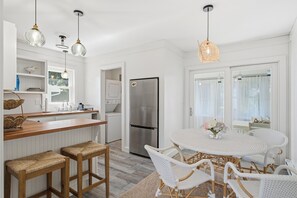 A modern kitchen with white cabinetry, a stainless steel refrigerator, and a round dining table with white wicker chairs.