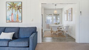 A room with a blue sofa, a dining table with chairs, and a painting of palm trees on the wall. - NEW Twin Tides Retreat-steps to private beach. Two Homes, One Memorable Stay (Clinton)