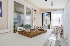 A dining area with a white table, wicker tray, white chairs, and a potted plant.