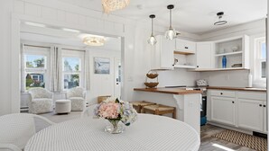 A modern kitchen with white cabinetry, a round dining table with a vase of flowers, and pendant lighting. - NEW Twin Tides Retreat-steps to private beach. Two Homes, One Memorable Stay (Clinton)