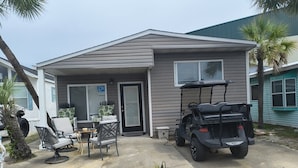 A single-story house with a front porch, a patio with outdoor furniture, and a golf cart parked in the driveway. - 2 Bedroom home with Golf Cart! (Panama City Beach)