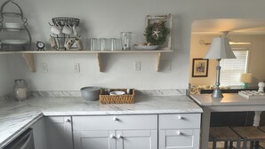 A kitchen with a marble countertop, white cabinetry, a hanging light fixture, and a small plant on the shelf. - 2 Bedroom home with Golf Cart! (Panama City Beach)