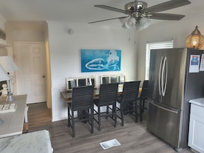 A kitchen with a stainless steel refrigerator, a dining table with chairs, a ceiling fan, and a wall-mounted painting. - 2 Bedroom home with Golf Cart! (Panama City Beach)