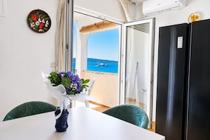 Ein Zimmer mit Tisch, Stühlen, einem Blumenstrauß, einem schwarzen Kühlschrank und Meerblick.
