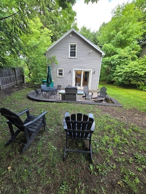 Una casa con un patio que tiene sillas tipo Adirondack, una parrilla y una pequeña mesa.