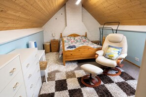 A bedroom with a sloped ceiling, a wooden bed, a white armchair, a dresser, and a checkered carpet. - 4-bed - Sleeps 8 - Free Parking (Leicester)