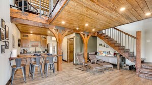 A spacious kitchen with wooden beams, a dining area with bar stools, a staircase, and a bed with a colorful headboard.