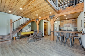 Un vaste espace de vie agrémenté d’un escalier en bois, une cuisine avec un coin bar et un espace repas.