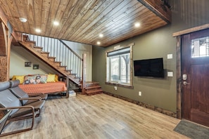 Quarto com escada de madeira, cama com roupa de cama colorida, TV fixada na parede e piso de madeira.