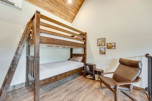 Uma cama beliche com escada de madeira, uma poltrona de couro marrom e uma pequena estante.