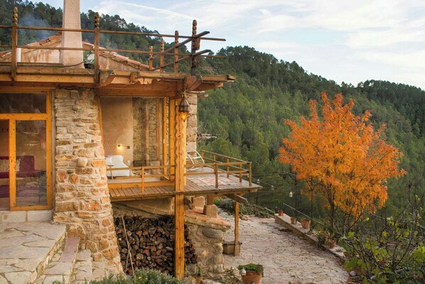 A stone building with a balcony, a fireplace, and a view of a forested hillside. - Farmhouse with pool, bath and spectacular views (Villahermosa del Río)
