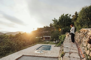A person standing by a stone pool with a view of a house and hills in the background.