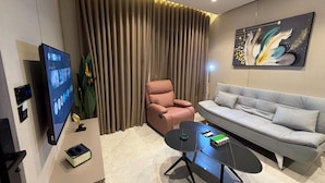 Een moderne woonkamer met een flatscreen televisie, een bank, een roze fauteuil, een salontafel en een groot schilderij aan de muur.