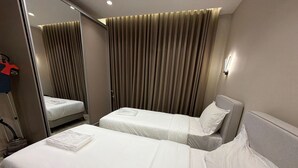 Een hotelkamer met twee bedden, een spiegel, een gordijn en een wandlamp.