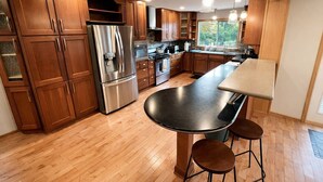 Une cuisine moderne avec des meubles en bois, des appareils en acier inoxydable, un grand îlot central avec des tabourets et un éclairage suspendu.