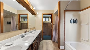 Ein Badezimmer mit Holzbalkendecke, einem großen Spiegel, zwei Waschbecken, einer Dusche und einer Tür zu einem weiteren Raum.