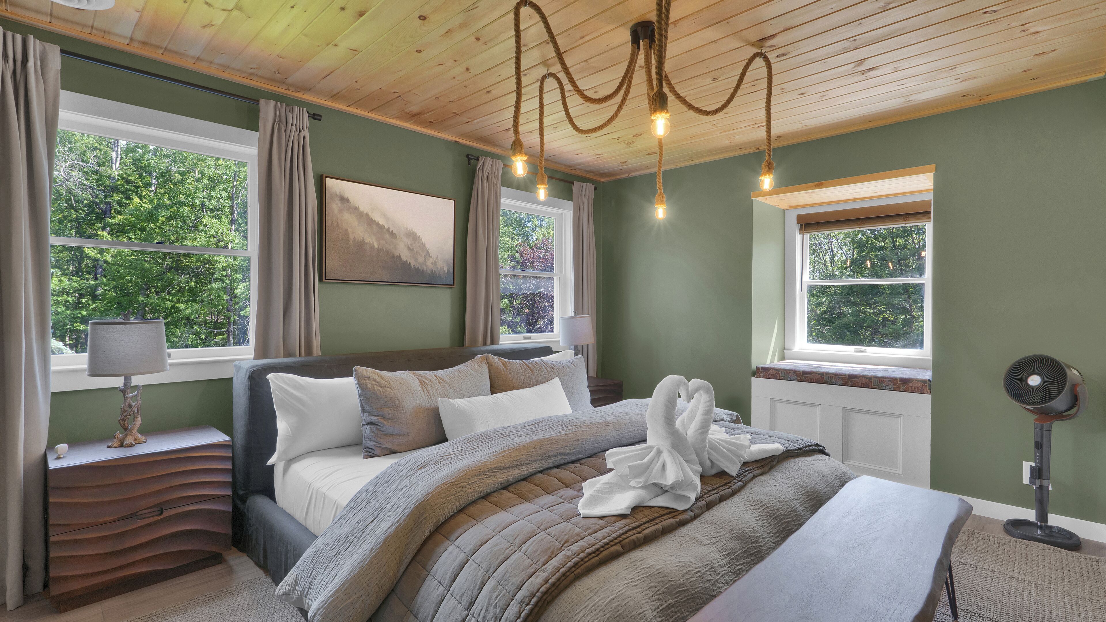 Un dormitorio con cama, mesitas de noche, una lámpara, un cuadro y una ventana con cortinas.