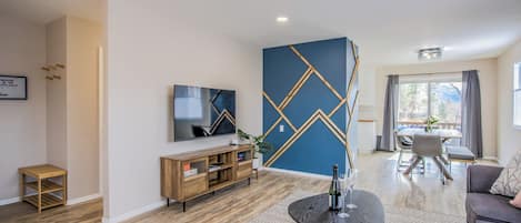 A modern living room with a TV, wooden entertainment unit, and a dining area with a table and chairs.