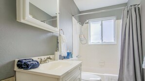 Ein Badezimmer mit weißem Waschtisch, Toilette, Dusche und einem Fenster mit Vorhang.