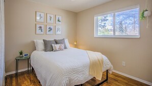 Ein Schlafzimmer mit einem Bett, einem Deckenventilator, einem Fenster mit Blick und gerahmten Pflanzenbildern an der Wand.