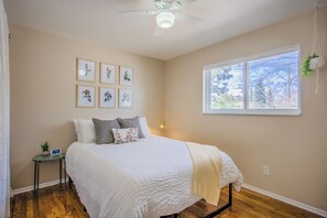 A bedroom with a bed, a ceiling fan, a window with a view, and framed botanical prints on the wall. - Delightful 4-bedroom house in Colorado Springs perfect for families (Colorado Springs)