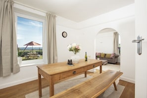 Ein Zimmer mit einem Holztisch, einer Bank, einer Vase mit Blumen, einer Weinflasche und Blick auf eine Terrassenanlage.