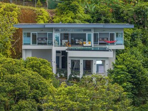 Ein modernes, zweistöckiges Haus mit einem Glasbalkon, umgeben von üppigem Grün.