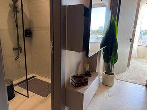 A modern bathroom with a glass shower enclosure, a vanity with a mirror, a potted plant, and a small shelf with books. - 406 Tara-jre Jabal Al Lweibdeh With Stunning View (Amman)