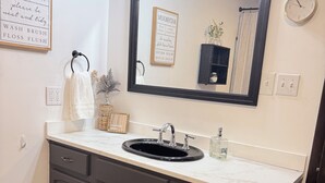 Une salle de bain avec un lavabo, un miroir et des placards. Il y a des panneaux sur le mur et une horloge.