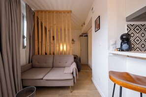 Een moderne woonkamer met een bank, een houten scheidingswand, een keuken met een koffiezetapparaat en een eetstoel.