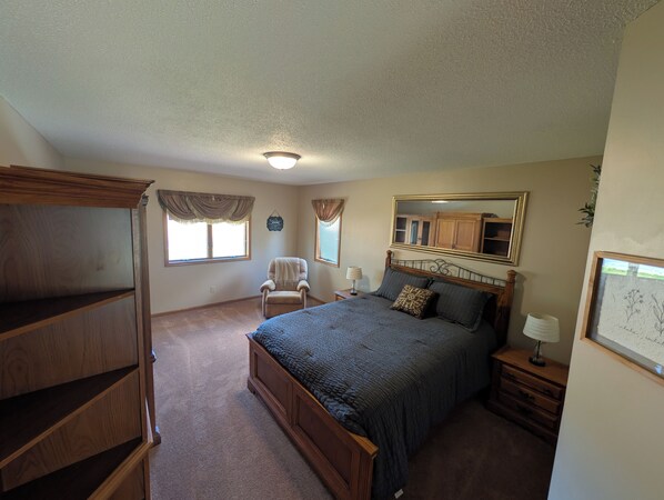 A bedroom with a bed, a chair, a dresser, a mirror, and a window.