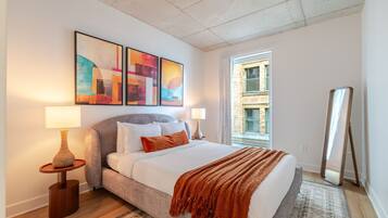 A bedroom with a bed, two bedside lamps, a rug, a window, and artwork on the wall.