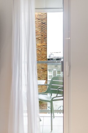 A balcony with a glass door, a brick wall, and a green chair. - Old Port 2BR | Pool Gym Parking (Montreal)